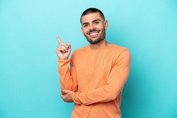 Young caucasian man isolated on blue background happy and pointing up