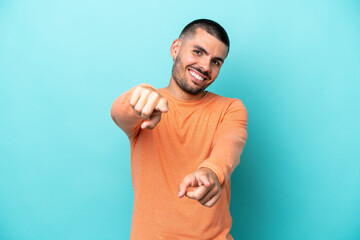 Young caucasian man isolated on blue background pointing front with happy expression
