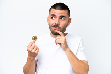 Young caucasian man holding a bitcoin isolated on white background having doubts and thinking