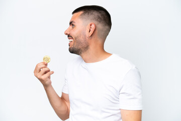 Young caucasian man holding a bitcoin isolated on white background laughing in lateral position