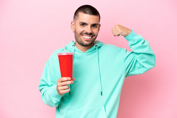 Young caucasian man holding soda isolated on pink background doing strong gesture
