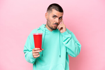 Young caucasian man holding soda isolated on pink background thinking an idea