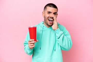 Young caucasian man holding soda isolated on pink background shouting with mouth wide open