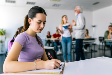 Focused young woman taking notes from books for her study. College student sitting at desk and...