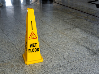 Wet floor caution sign on walkway in modern building. Warning red slip and fall people and text "WET FLOOR", sign on yellow plastic rubber cone on granite floor inside the building with copy space.