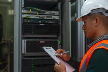 an asian man IT technician working on network Internet cables and servers and try to checklist on the paper board to maintenance the data sharing network