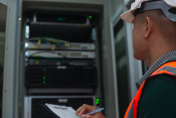 an asian man IT technician working on network Internet cables and servers and try to checklist on the paper  board to maintenance the data sharing network