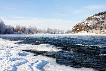 A frozen river bank with a distant mountain under a cloudy sky