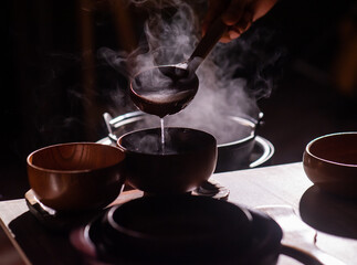 Silhouettes in a retro-style restaurant as a cook ladles hot food with a wooden ladle into wooden cups.