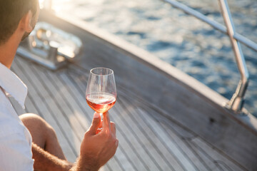 Drinking wine on yacht at sea. Travel in summer vacation, picnic at sunset. Wineglass of...