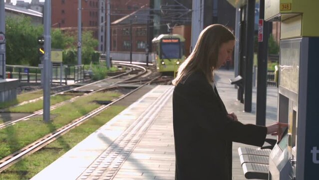 woman buys a tram ticket at a ticketing machine and at that moment the tram arrives at the stop