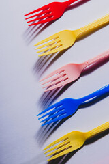 flat lay of  5 five Multicolored party plastic forks arranged side by side with hard shadow over white background