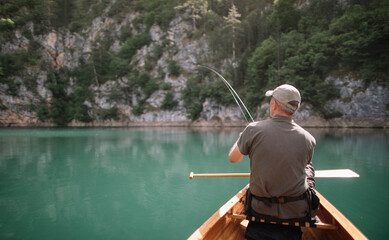 Rear view of man fishing from canoe on sunny day, copy space