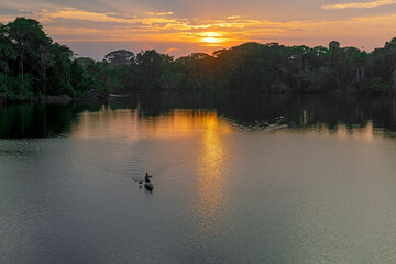 Unrecognizable Indigenous Quechua man riding canoe at sunrise, Amazon Rainforest, Yasuni national park, Ecuador.