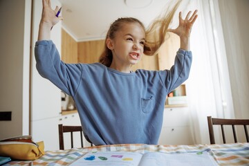 A first-grader emotionally laughs, shouts and gets angry while doing her homework at home in the...