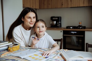 A young mother helps her first-grader daughter do her homework at home in the kitchen