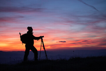 Silhouette of a photographer on top of a hill watching beautiful sunset. 