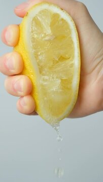 Hand squeezing lemon juice from half a lemon on a white background slow motion.