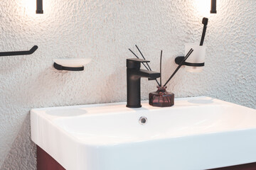 A bathroom sink with a black faucet and a white soap dish. A bottle of perfume is on the counter...