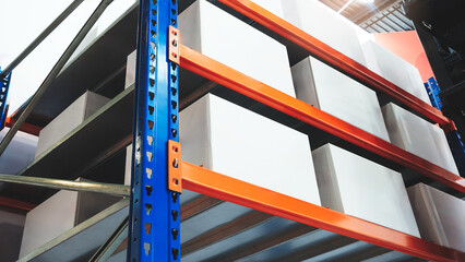 A stack of white boxes in warehouse on a blue and orange rack. The boxes are stacked on top of each...