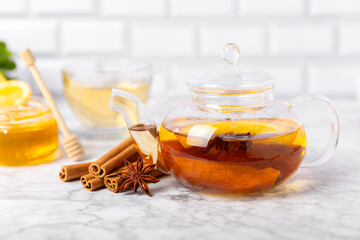 Fragrant hot tea with cinnamon stick and anise on a textured wooden background. A teapot brewing hot tea with honey, lemon, mint and apples. Spicy tea with spices. Immunity tea. Health concept.