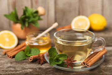 Fragrant hot tea with cinnamon stick and anise on a textured wooden background. A cup of hot tea with honey, lemon, mint and apples. Spicy tea with spices. Immunity tea. Health concept.Copy space.
