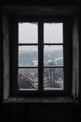 Fototapeta premium A window in an abandoned building offers a view of a distant town on a dark, misty winter's day.