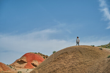 Obraz premium Magnificent landscape of the red hills in Georgia, a young man on a high ridge against the blue sky, a poster for advertising tours with copy space for advertising
