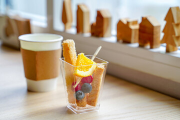 A collection of fruits, oranges, grapes, cherries, hard bread in a clear glass, healthy items on a wooden table by the window, looks warm and refreshing.