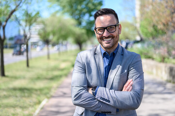 Portrait of handsome professional with arms crossed smiling and standing in city during sunny day