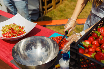 Hands of a woman in disposable gloves dicing ripe strawberries to make jam, jam or pie in the garden. The process of cooking summer dishes with fresh fruit