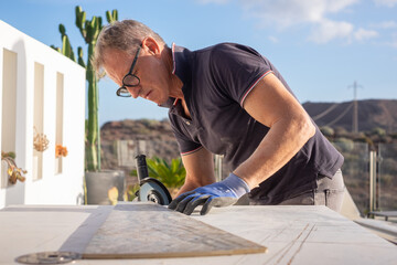 Caucasian worker with gloves holding an angle grinder for cutting metal, stone and ceramic. Man cutting a piece of ceramic plate with a typewriter