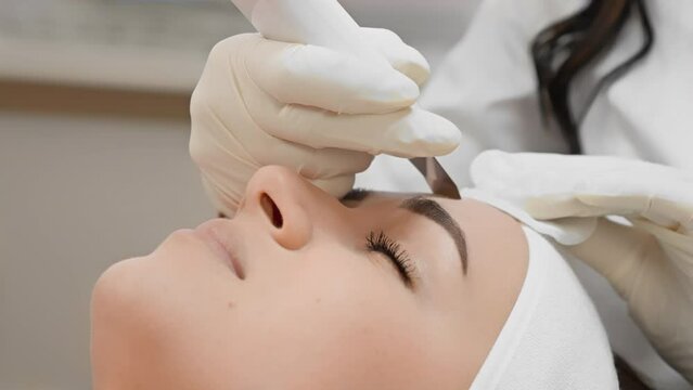 At a beauty clinic, a woman is getting eyebrow microblading by a skilled artist with precision. The meticulous treatment enhances her brows, ensuring a professional and aesthetic look
