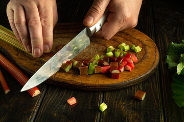 Slicing rhubarb with a knife in the hand of a chef to prepare a delicious vegetable menu on the...