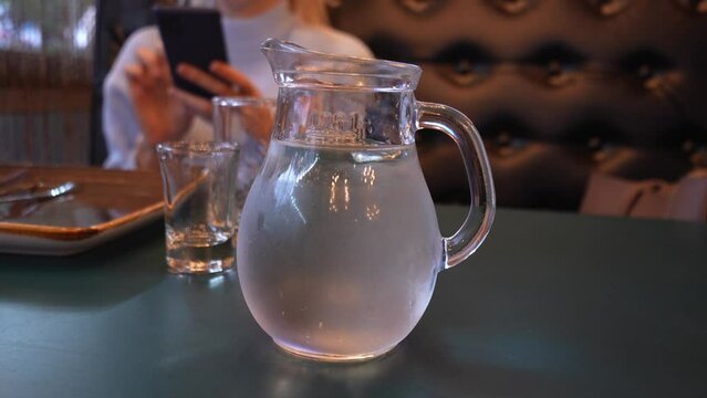 Close-up of small decanter of vodka or chacha covered in drops of water on table in restaurant. Selective focusing. Vodka in decanter and glass on wooden plank table. Bar atmosphere with drinks