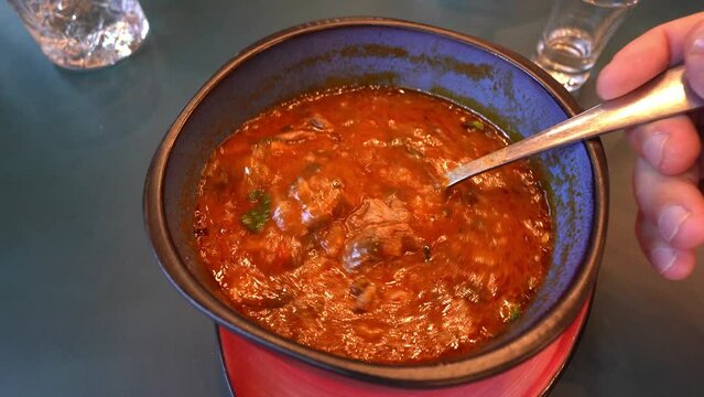 Georgian soup. Kharcho with rice, tomatoes, beef, garlic and herbs in bowl on wooden table Traditional Caucasian food spicy soup with lamb, tkemali and rice. Man showing pieces of meat with spoon.
