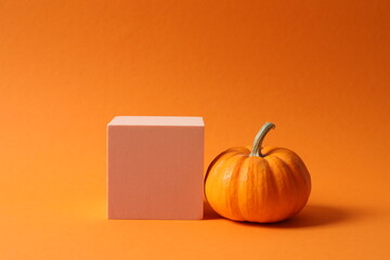 Small orange pumpkin on a white podium with copy space. Halloween or Thanksgiving celebration concept.