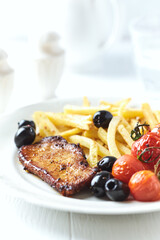 Roast Pork Steak with french fries, tomatoes and olives. White wooden background. Close up.