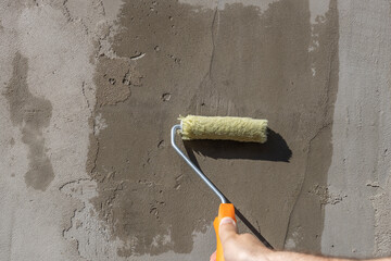 applying a primer to the wall with a yellow roller, showing the process of improving and repairing...