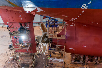 Cargo vessel in dry dock on ship repairing yard. Variable pitch propeller and rudder. Welder...