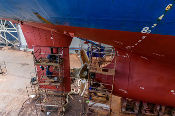 Cargo vessel in dry dock on ship repairing yard. Variable pitch propeller and rudder. Welder...