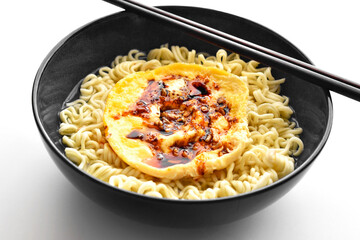 Instant noodles with egg, seasonings and soy sauce with chopsticks in a black bowl. 