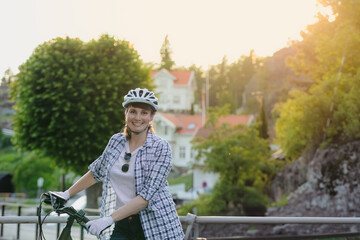 Mature woman in helmet happy smiling standing with her bicycle in a scenic area at sunset. Suitable...