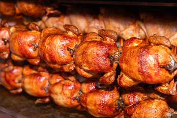 Multiple chickens cooking on a rotisserie spit, crispy and golden, in a commercial kitchen