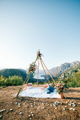 Wedding wigwam arch with a blanket and pillows stands in a clearing on a mountain above the Bay of...