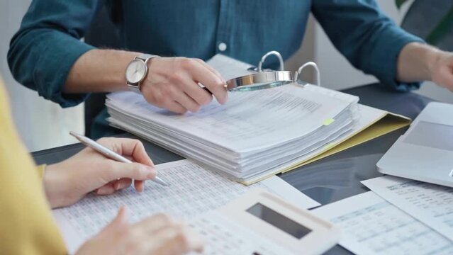 Businessman or professional auditor is analyzing data sheets. Close-up of an bookkeeper's hand with magnifying glass inspecting financial reports. Business audit and taxes