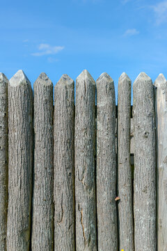 A closeup of an old faded wooden wall at a fort. The tops are sharpened. Blue sky above. Portrait orientation.