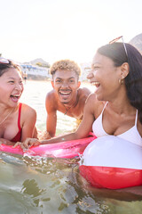Vertical. Three multiracial young people in swimwear laughing looking each other enjoying inside...