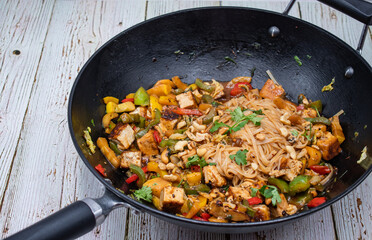 Vegan pepper, tofu and zucchini stir fry in wok, wooden table,