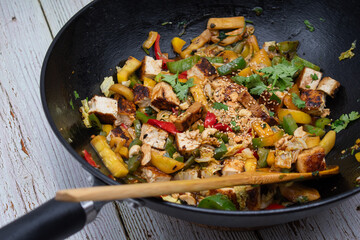 Vegan pepper, tofu and zucchini stir fry in wok, wooden table,